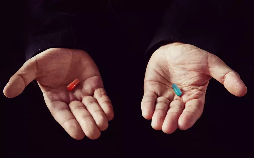 Hands holding both a red pill and a blue pill