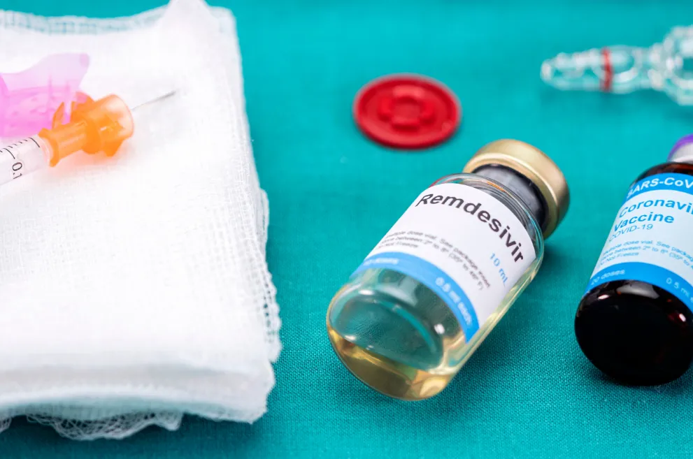 Remdesivir vial next to COVID vaccine and syringe