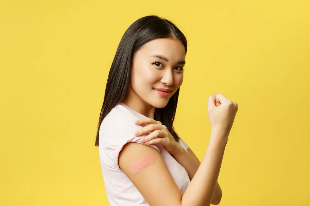 Young woman flexing arm with bandaid after vaccine