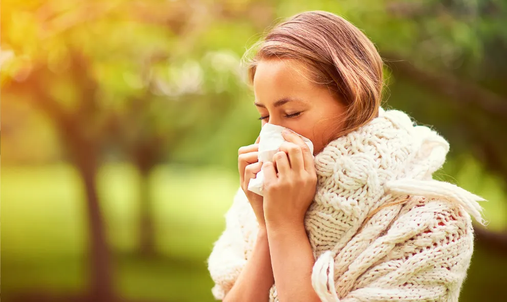 A woman blowing her nose outside among the trees
