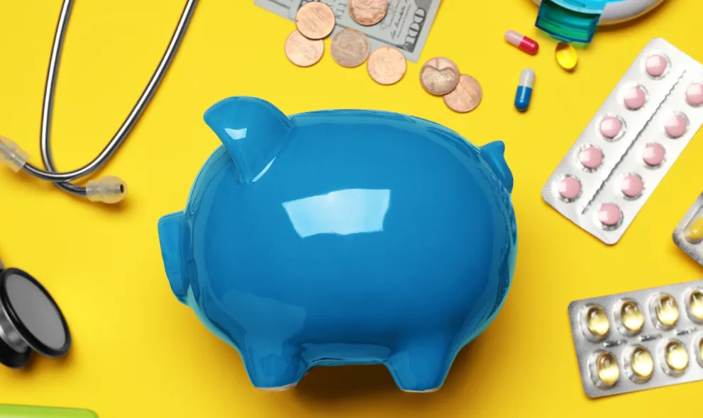Blue piggybank with money, medications and stethoscope on yellow background
