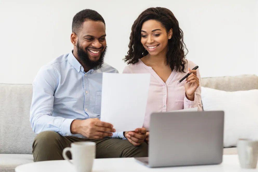 Couple on sofa looking at paper with laptop nearby