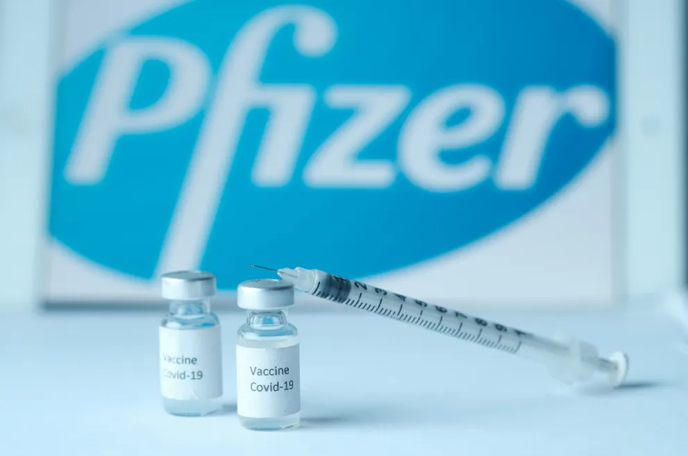COVID vaccine vials and syringe in front of Pfizer logo