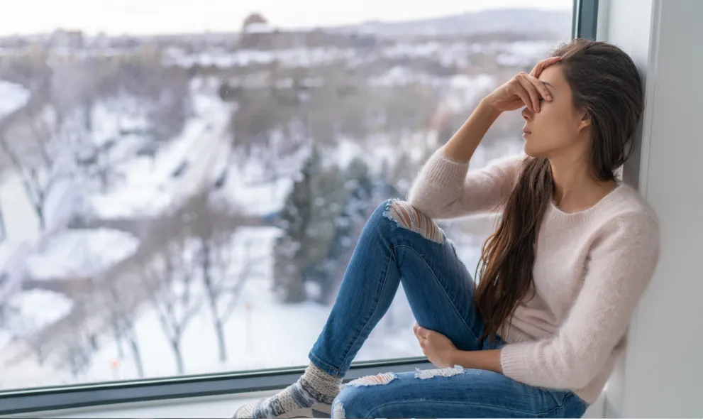Depressed woman sitting by the window during winter