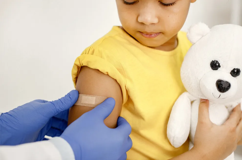 Doctor placing bandage on child holding teddy bear