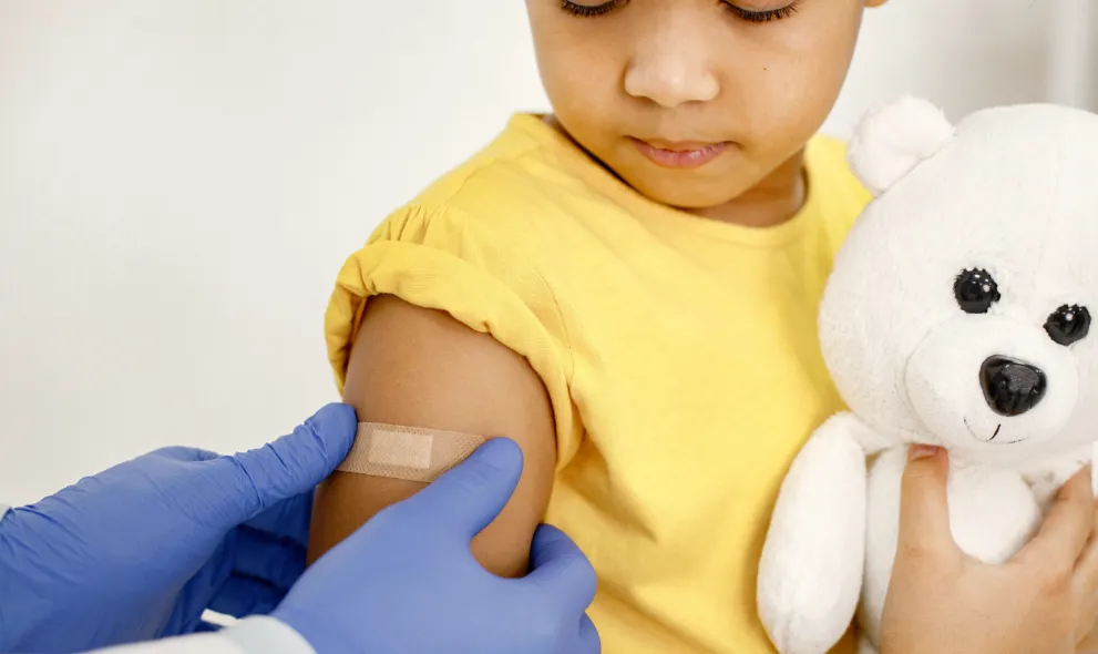 Doctor putting band-aid on the arm of girl after vaccine