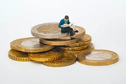 Small clay man sitting on stack of coins