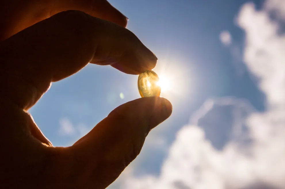 Hand holding vitamin d capsule in front of sun