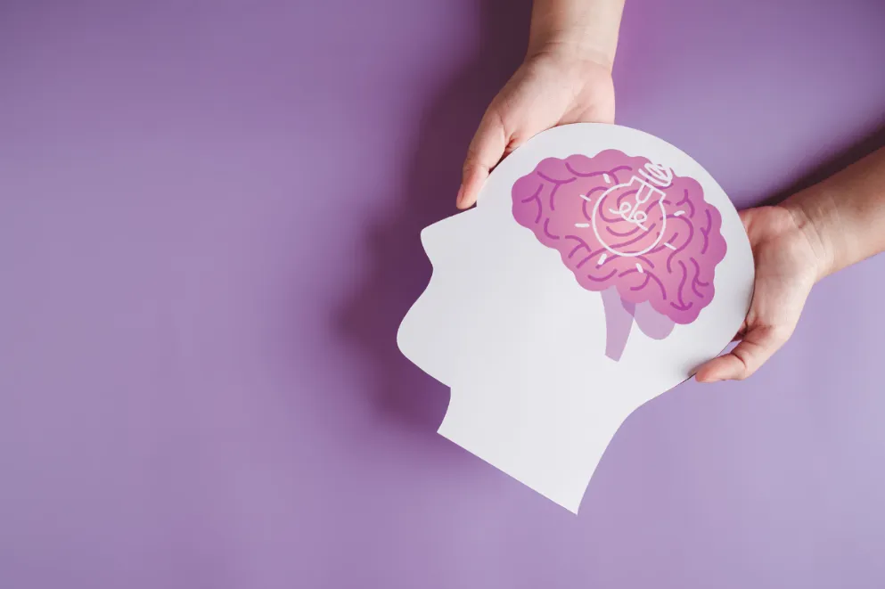 Hands holding paper cutout of head with brain and light bulb