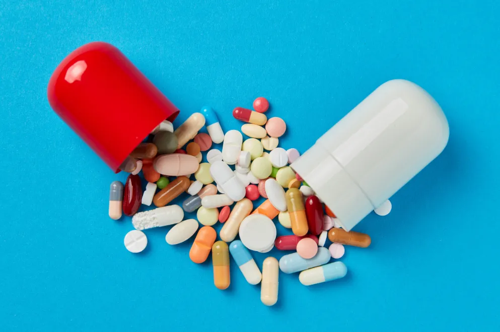 Large pill spilling out other medicines on blue background
