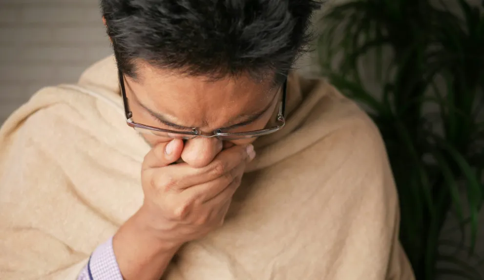 Man in brown sweater coughing
