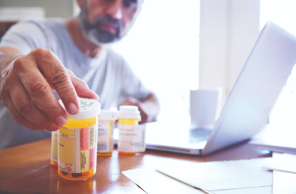 Man sitting at laptop looking a prescription bottles