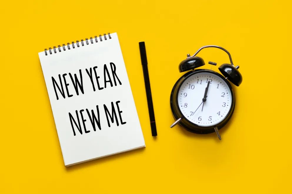 Notepad reading new year new me with pen and clock on yellow background