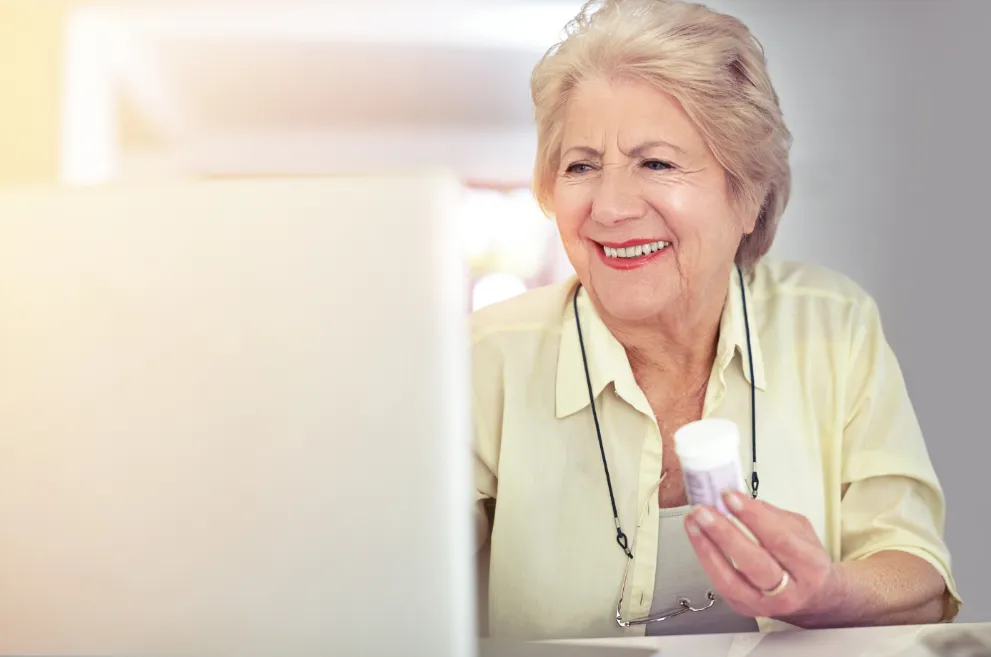 Older woman holding pill bottle and using computer