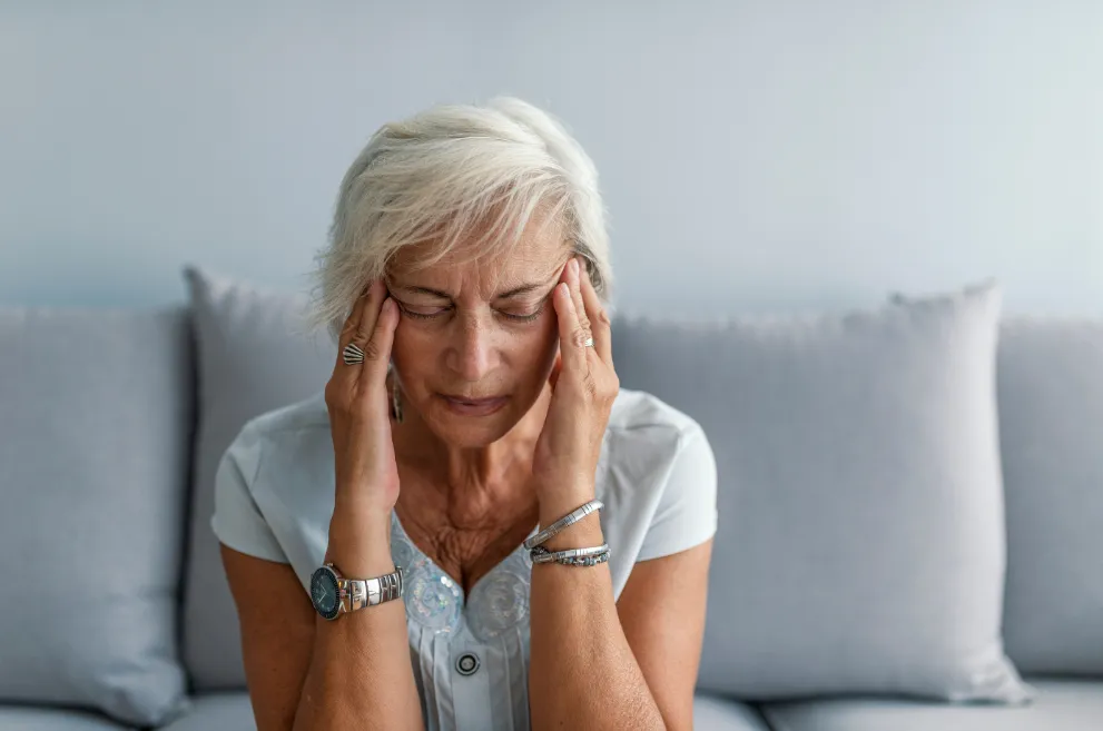 Older woman sitting on sofa and rubbing her temples