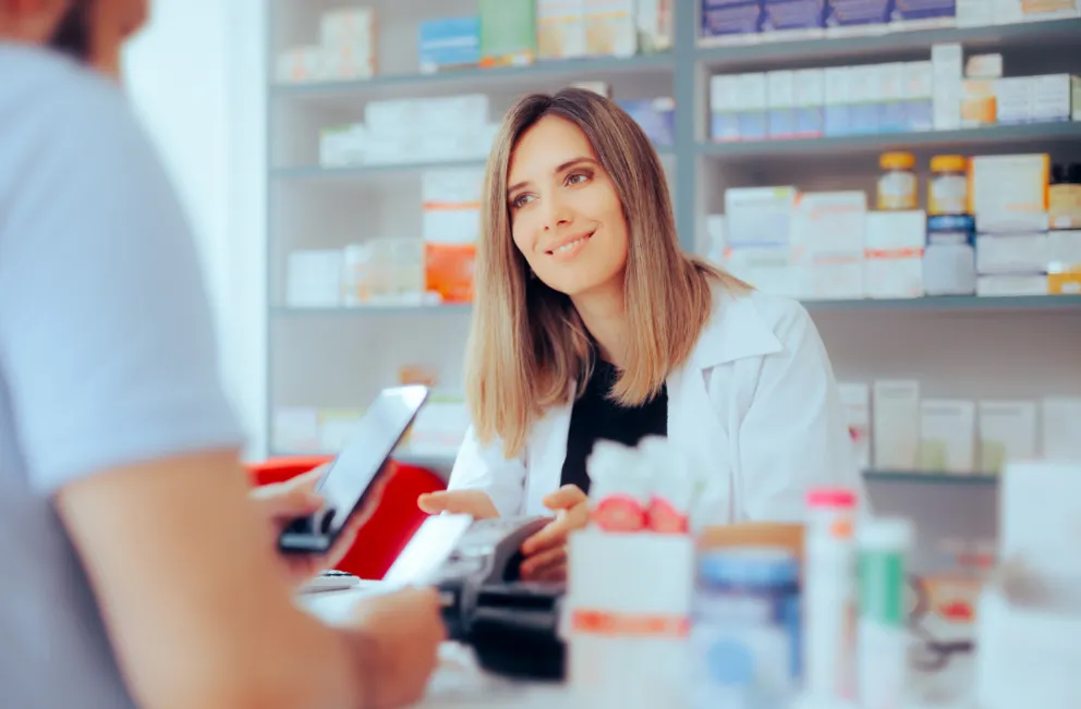 Patient standing at pharmacy counter with pharmacist looking at coupon on phone