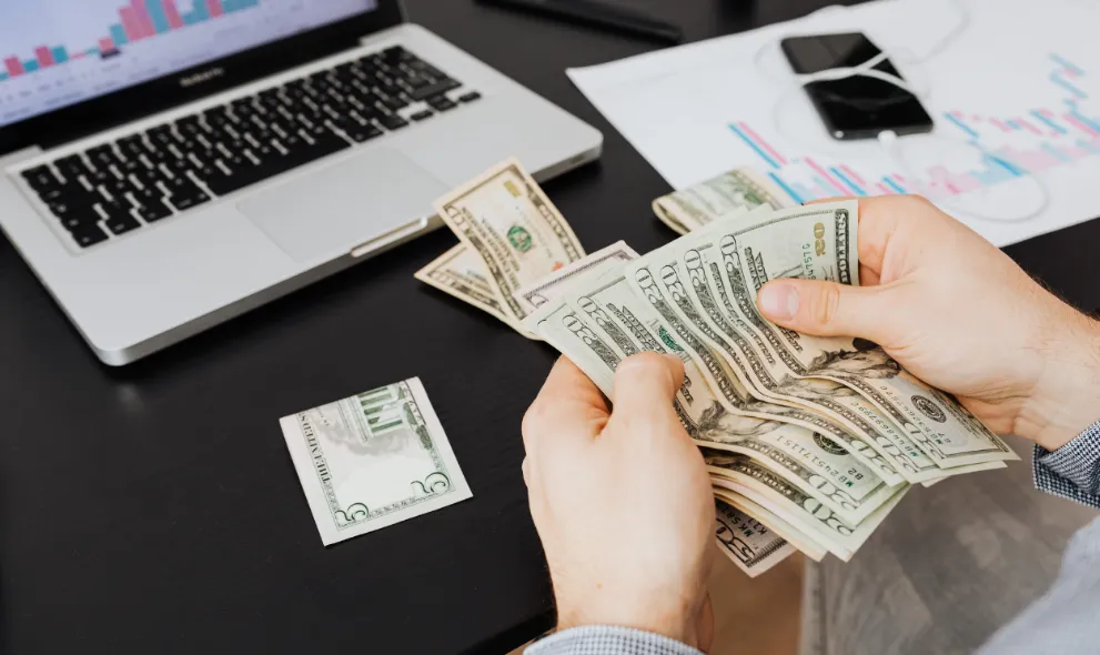 Person counting money while using a laptop