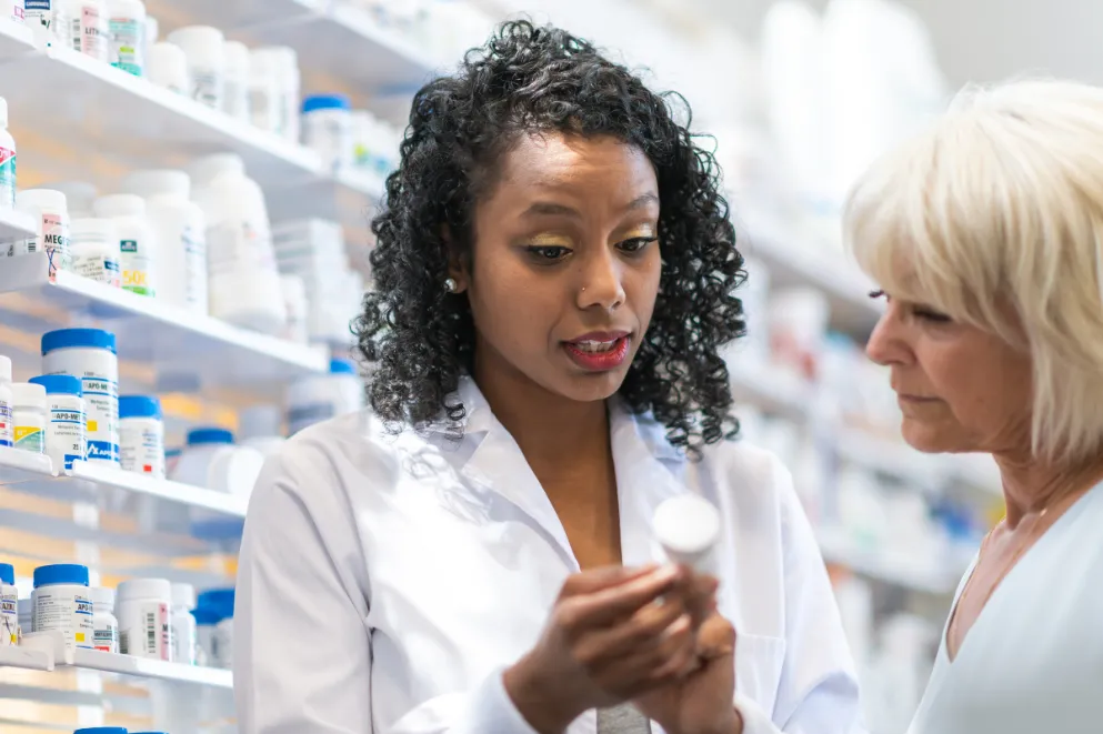 Pharmacist holding pill bottle and talking to customer