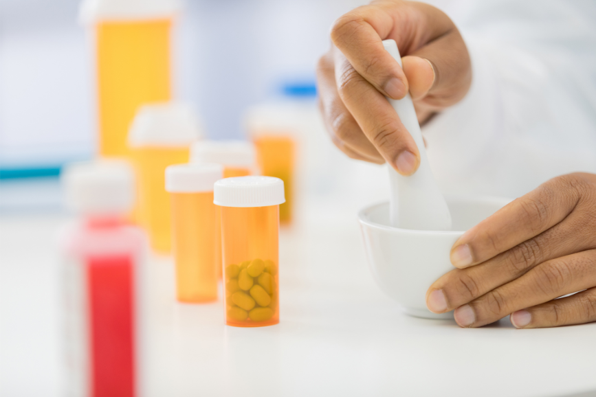 Pharmacist using mortar and pestle with pill bottles