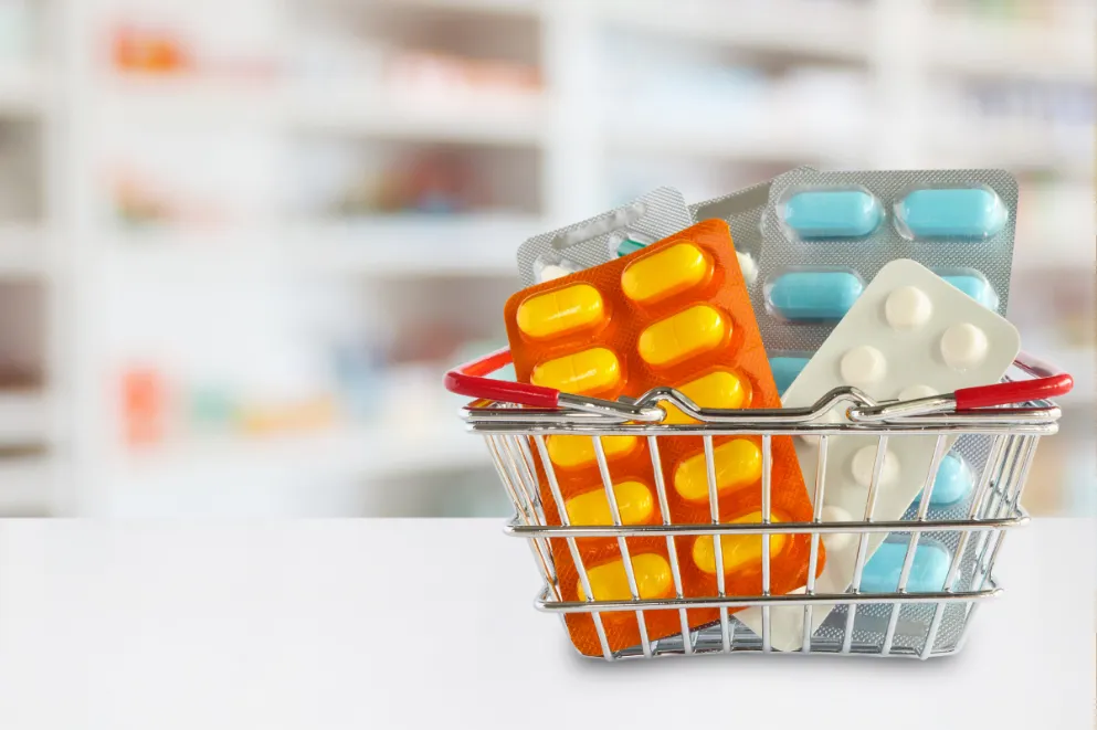 Pills in mini shopping basket with pharmacy in background