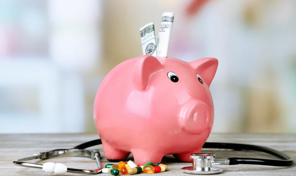 Pink piggy bank with stethoscope and pills
