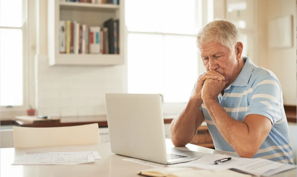 Senior man reviewing finances on laptop in kitchen