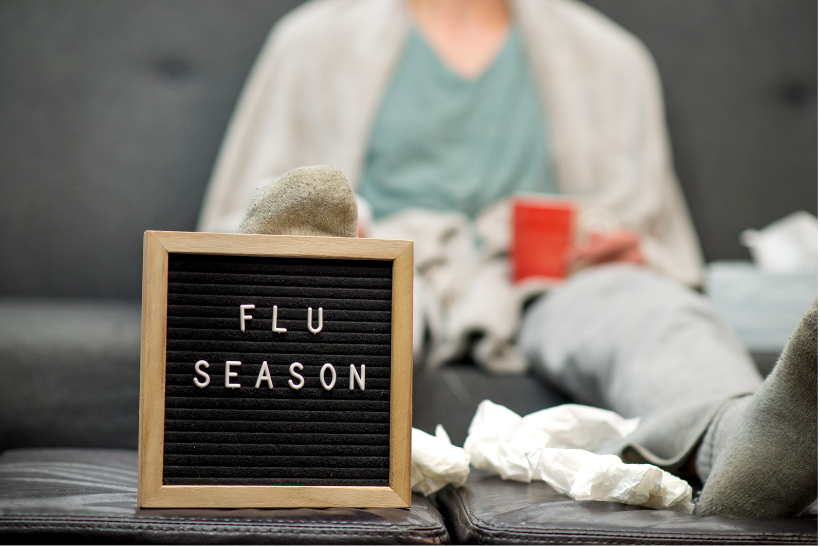 Sick person on couch with a sign that says Flu Season