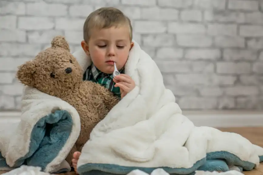 Sick toddler with thermometer and teddy bear