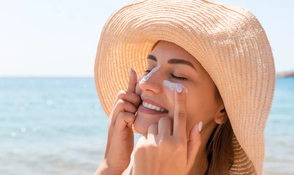 Smiling woman in hat applying sunscreen to her face