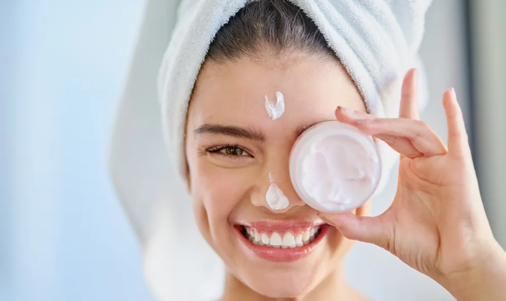 Smiling young woman applying moisturizer to her skin