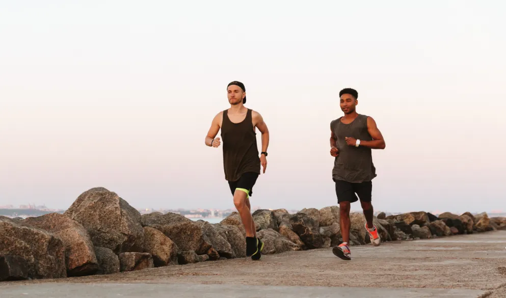 Two young fitness men running outdoors at the beach