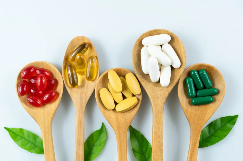 Vitamins in wooden spoons on light background