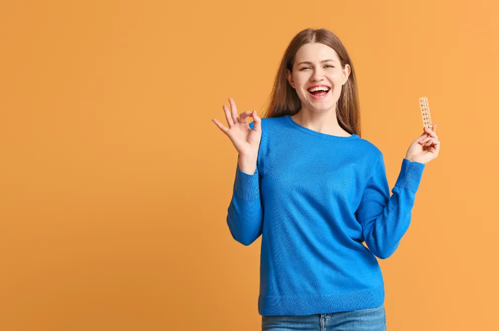 Woman holding pack of pills and smiling on orange background