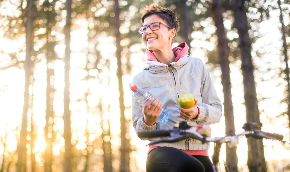 Woman riding a bike holding a water bottle and apple