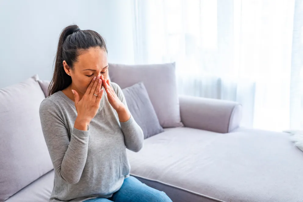 Woman sitting on sofa rubbing her sinuses