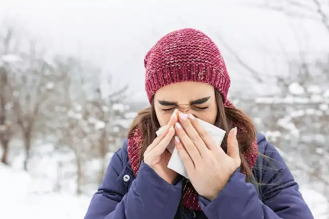 Woman sneezing outside in snow