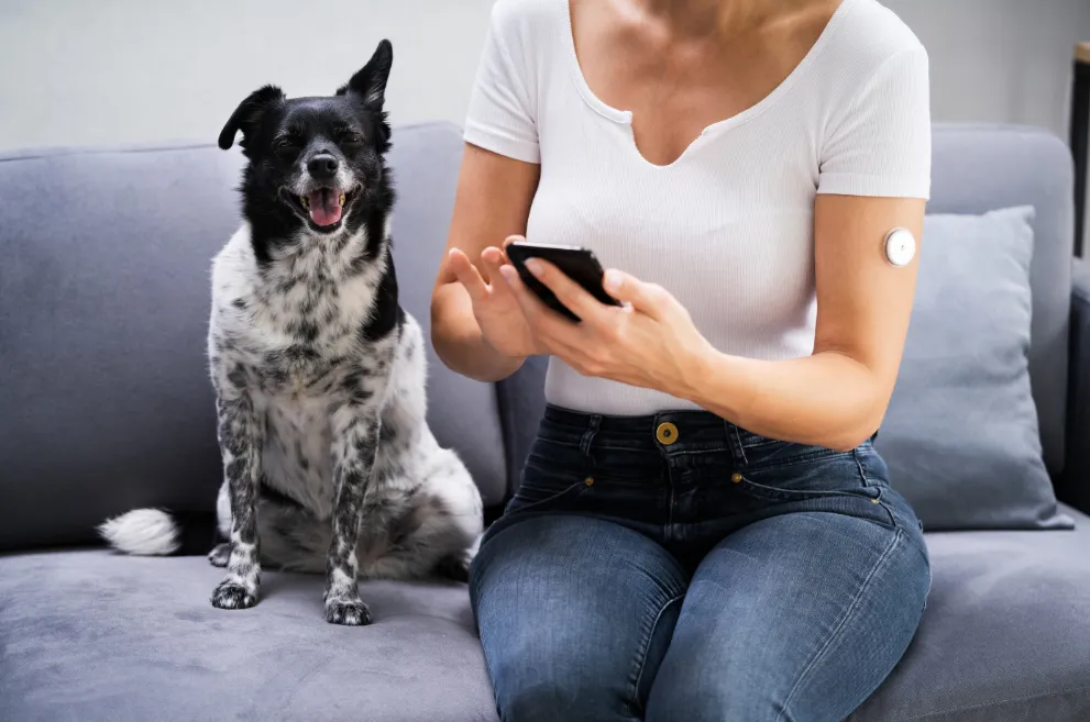 Woman wearing glucose meter and holding phone next to dog