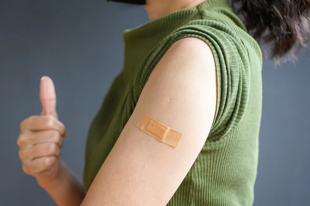 Woman with bandaid on arm giving thumbs up