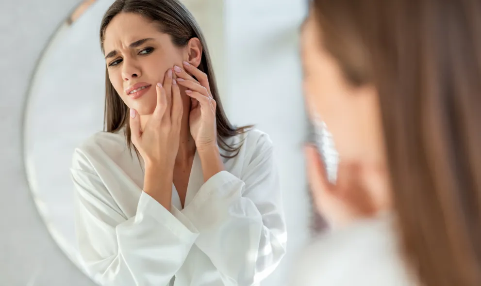 Young woman popping pimple in front of mirror